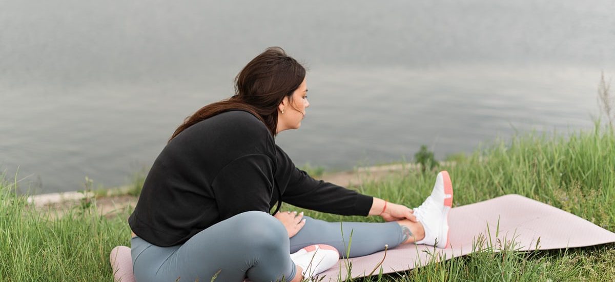 A woman stretches on a yoga mat by a serene lake, embodying relaxation and wellness in nature.