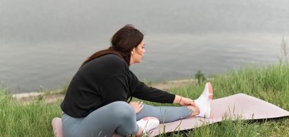 A woman stretches on a yoga mat by a serene lake, embodying relaxation and wellness in nature.